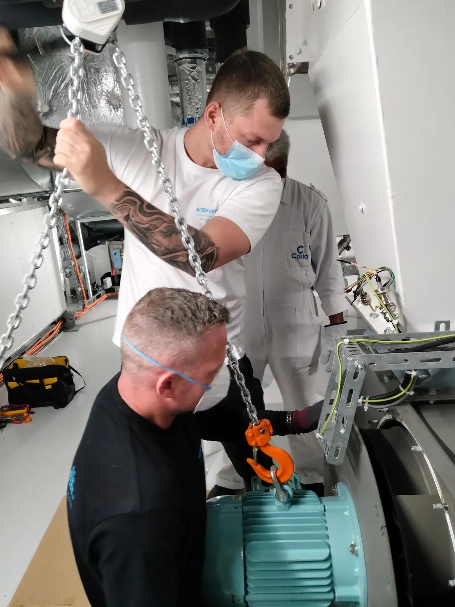 Two technicians lifting a fan motor with a chain hoist